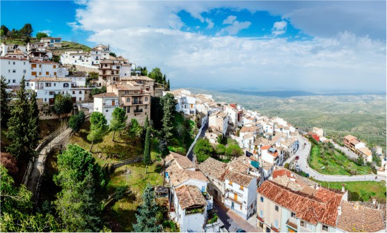 Vista panorámica del valle del olivo tomada desde lo alto de la montaña del pueblo de La Iruela. En ella se ven las casas de poca altura subiendo por la ladera de la montaña y en el fondo de la imagen los campos de cultivo. 