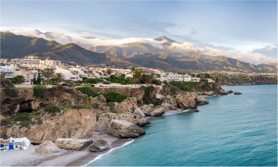 Hermoso paisaje costero de la localidad de Nerja con acantilados, mar en calma y fondo con montañas con nubes bajas. 