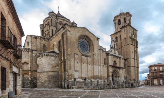Imagen de la Iglesia Colegiata de Santa María la Mayor en Toro de estilo románico-gótico en la que se ve parte de su fachada con un enorme rosetón y el campanario. Detrás de este sobre sale el cimborrio, una impresionante cúpula sobre tambor octogonal, que recuerda al de la Catedral de Zamora y la Catedral Vieja de Salamanca. 