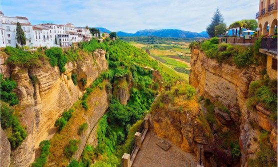 Vista panorámica de la espectacular ciudad de Ronda situada en lo alto del precipicio del desfiladero. Las casas son de color blanco y en el fondo de la imagen se ven los prados verdes. 