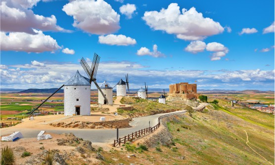 Molinos de viento y fortaleza en la localidad de Consuegra, una llanura entre campos de cultivo en la que se encuentran los molinos de viento encalados con los techos en tonos grises y grandes aspas.   
