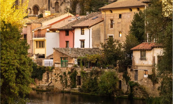 Bonita imagen de la ciudad de Estella. La fotografía ha sido tomada desde el Río Ega, con una vista panorámica del Convento de Santo Domingo rodeado por edificios antiguos de color salmón, amarillo, blanco, así como otros construidos en piedra entre plantas de diferentes tonos verdes y amarillos. Una imagen de aspecto rural. 
