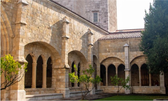 Imagen del claustro de la basílica de la Asunción de Santander de estilo gótico, formado por grupos de varios arcos envueltos externamente por un gran arco escarzano. Detrás del claustro se alza robusta una torre hexagonal  