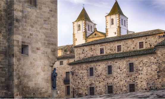Imagen del centro de la ciudad medieval de Cáceres. En segundo plano destacan las dos torres blancas de la iglesia de San Francisco Javier y en primer plano, parte de una plaza empedrada desde la que ha sido tomada la fotografía, con las fachadas de casas empedradas y parte de la Concatedral de Santa María con las escultura de bronce de San Pedro de Alcántara en una de las esquinas 