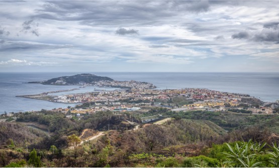 Vista aérea de Ceuta tomada desde un montículo desde donde se ve parte de la ciudad y su puerto con zonas verdes y urbanizadas.